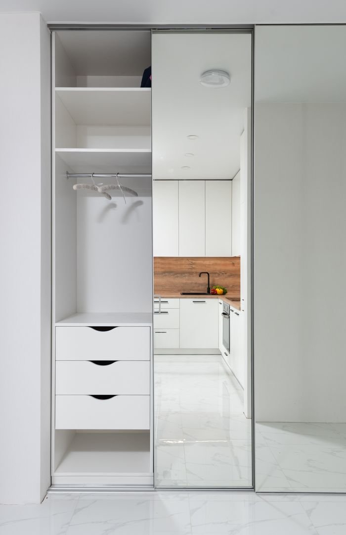 about-us-02 Wardrobe in hallway with mirrored wall reflecting furniture of modern kitchen in light apartment